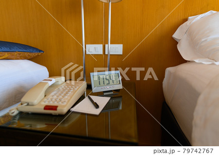 A digital clock is placed on a bedside table with wooden walls 79742767