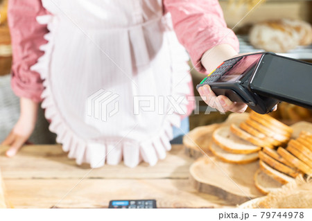 The shop assistant accepts payment via the mobile phone for the sold bread. Cashless payment in the bakery store. 79744978