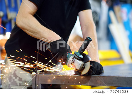 Metalwork craftsman cutting metal with grinder tools. Worker man in protection gloves and glasses working in the workshop. Small local business. 79745583