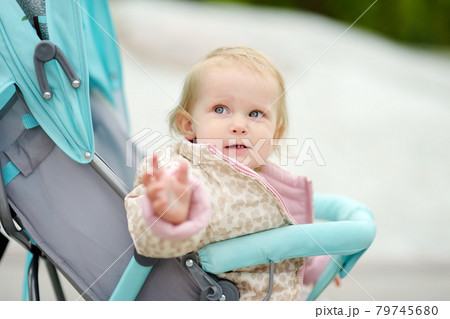 Adorable toddler girl is riding into baby stroller during stroll. Active leisure for family with little kids. Happy childhood. 79745680