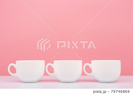 Three white ceramic cups in a row on white table against pink background Three white ceramic cups in a row on white table against pink background 79746869