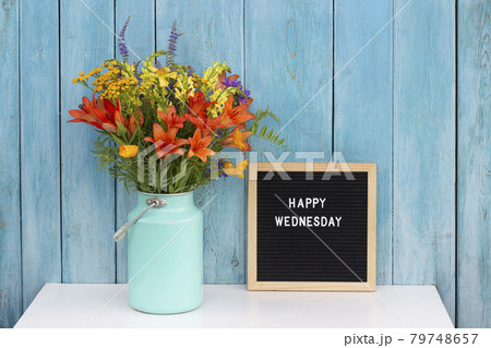 Happy Wednesday words on black letter board and bouquet of bright wildflowers in tin can vase on table against blue wooden wall. Concept Hello Wednesday Happy Wednesday words on black letter board and bouquet of bright wildflowers in tin can vase on table against blue wooden wall. Concept Hello Wednesday 79748657