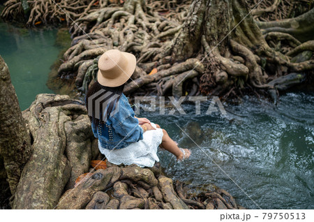 A woman swaying her feet in the water with the beautiful root of trees A woman swaying her feet in the water with the beautiful root of trees 79750513
