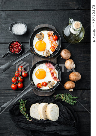 Fried eggs with cherry tomatoe and bread for breakfast in cast iron frying pan, on black wooden table background, top view flat lay Fried eggs with cherry tomatoe and bread for breakfast in cast iron frying pan, on black wooden table background, top view flat lay 79755278