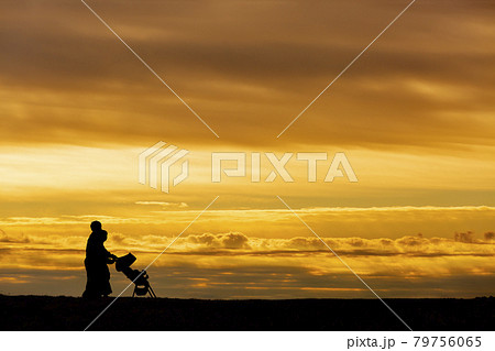 夕日の空を背景にベビーカーを押し散歩をする若い夫婦 夕日の空を背景にベビーカーを押し散歩をする若い夫婦 79756065