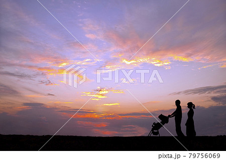 夕日の空を背景にベビーカーを押し散歩をする若い夫婦の写真素材