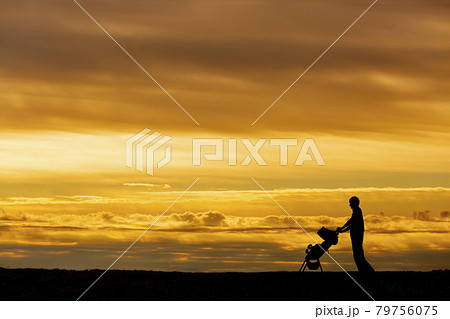 夕日の空を背景にベビーカーを押し散歩をする若い男性の写真素材