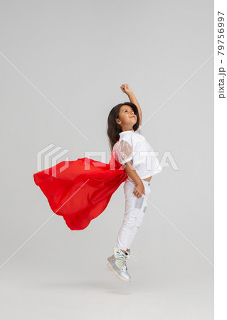 Small superhero. Little cute Caucasian girl in a red cape isolated over white studio background. Side view 79756997