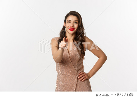 Elegant woman in glamour shiny dress pointing finger at you, concept of christmas holidays and party, standing over white background 79757339