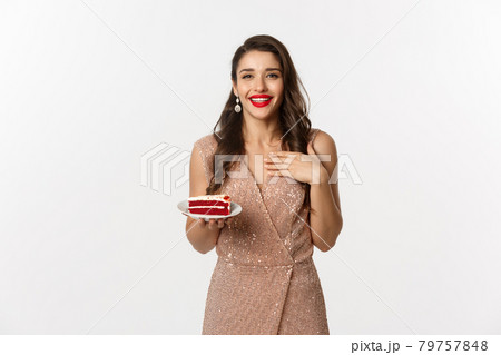 Party and celebration concept. Attractive slim woman in elegant dress holding piece of cake and smiling, standing over white background 79757848