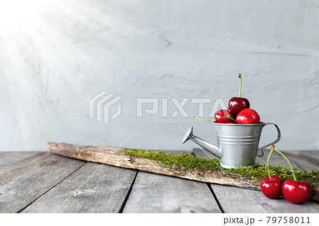 Sweet cherry berries in watering can on wooden background table, gray wall Sweet cherry berries in watering can on wooden background table, gray wall 79758011