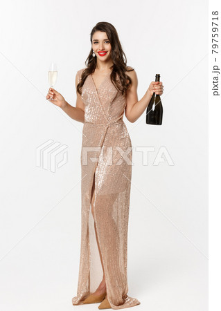 Christmas party and celebration concept. Full length of elegant woman with red lips, luxury dress, holding glass of champagne and bottle, white background 79759718