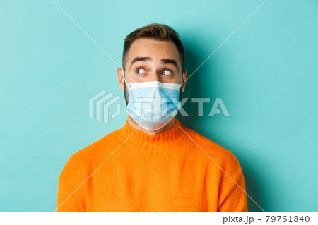 Covid-19, social distancing and quarantine concept. Close-up of young male model in medical mask looking left curious, staring at promo copy space, light blue background Covid-19, social distancing and quarantine concept. Close-up of young male model in medical mask looking left curious, staring at promo copy space, light blue background 79761840