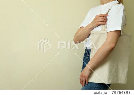 Young woman in blank t-shirt with bag against beige background Young woman in blank t-shirt with bag against beige background 79764393