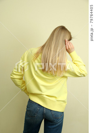 Young woman in yellow sweatshirt against beige background Young woman in yellow sweatshirt against beige background 79764405