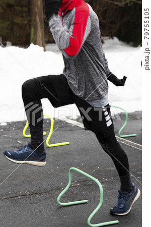 Runner stepping over mini hurdles in a parking lot because of a snow storm Runner stepping over mini hurdles in a parking lot because of a snow storm 79765105