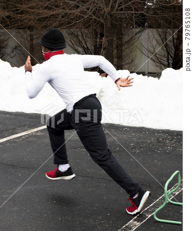 Fast runner running over mini hurdles in a parking lot with snow 79765108
