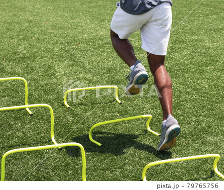 Young runner running over yellow mini hurdles on a turf field 79765756