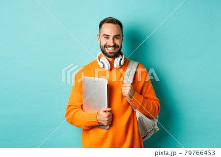 Happy man with backpack and headphones, holding laptop and smiling, going to work, standing over turquoise background 79766453
