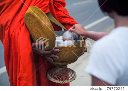 Rear view of girl puts the food into the bowl of monk during making the merit 79770245