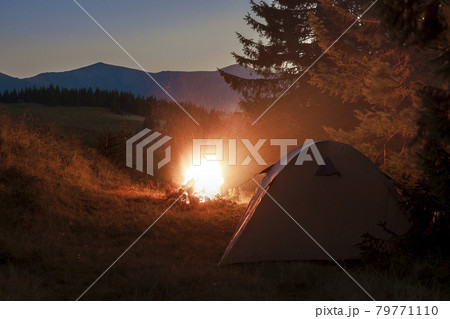 Hikers tent in mountains at evening with a bonfire with sparkles near it 79771110