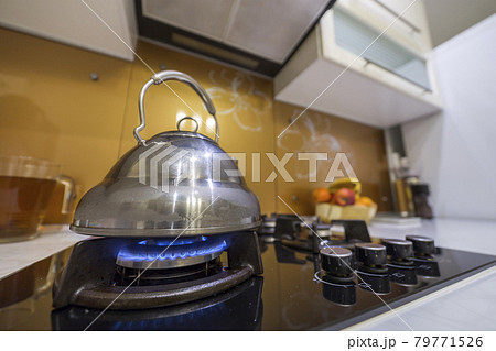Shiny stainless tea kettle teapot with boiling water on burning gas stove on modern kitchen yellow interior background. 79771526
