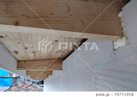 Installation of wooden beams of roof frame with spray foam on a house wall under construction. Installation of wooden beams of roof frame with spray foam on a house wall under construction. 79771958