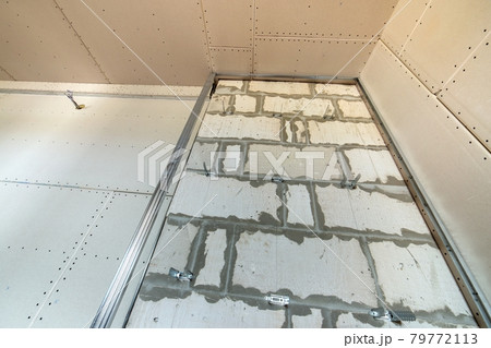 Unfinished brick wall in a room under construction prepared for drywall plates frame installation. Unfinished brick wall in a room under construction prepared for drywall plates frame installation. 79772113
