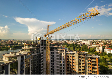 Apartment or office tall building under construction. Brick walls, glass windows, scaffolding and concrete support pillars. Tower crane on bright blue sky copy space background. Apartment or office tall building under construction. Brick walls, glass windows, scaffolding and concrete support pillars. Tower crane on bright blue sky copy space background. 79772220