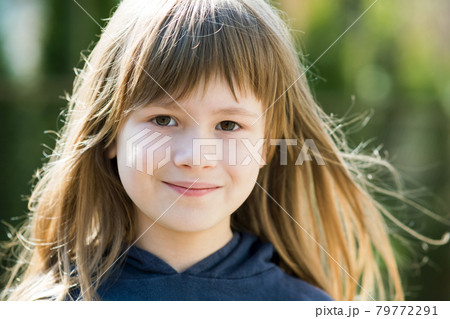 Portrait of pretty child girl with gray eyes and long fair hair smiling outdoors on blurred bright background. Cute female kid on warm summer day outside. 79772291