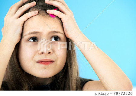 Close up portrait of upset and pensive little girl with cute pink hairpin on blue background. 79772526