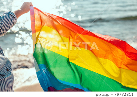 Young person hand with a colorful rainbow flag on blue background. Young person hand with a colorful rainbow flag on blue background. 79772811