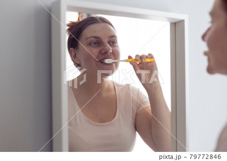 Portrait of beautiful millennial woman brushing teeth looking in mirror during morning hygiene procedures in the bathroom. Hygiene, dental care concept. 79772846