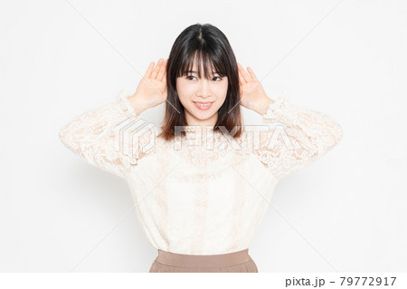 白背景の前に立って、聞き耳を立てる、レースのブラウスを着た若い女性 79772917