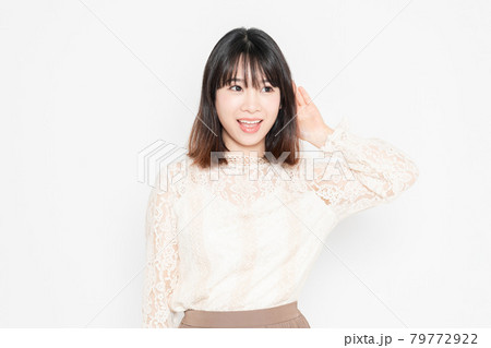 白背景の前に立って、聞き耳を立てる、レースのブラウスを着た若い女性 79772922