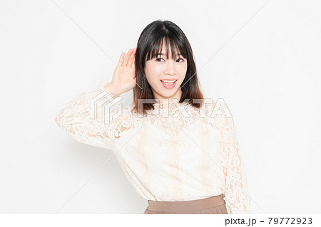 白背景の前に立って、聞き耳を立てる、レースのブラウスを着た若い女性 白背景の前に立って、聞き耳を立てる、レースのブラウスを着た若い女性 79772923