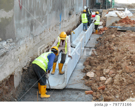 MALACCA, MALAYSIA -JANUARY 31, 2017: Drainage work by construction workers. Construction workers installing precast u-shape concrete drain at the construction site. MALACCA, MALAYSIA -JANUARY 31, 2017: Drainage work by construction workers. Construction workers installing precast u-shape concrete drain at the construction site. 79773166