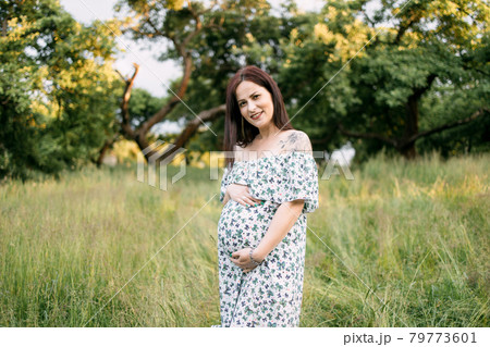 Charming pregnant woman in summer dress posing outdoors 79773601