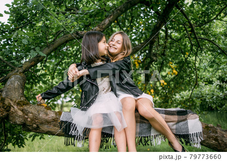 Joyful sisters sitting in embrace on branch of old tree 79773660