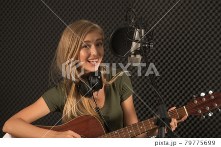Young beautiful female musician with guitar is testing the sound system in the recording studio before taking part in the recording. 79775699