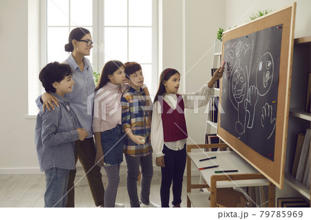 Elementary school girl student answering at board on lesson front of classmates Elementary school girl student answering at board on lesson front of classmates 79785969
