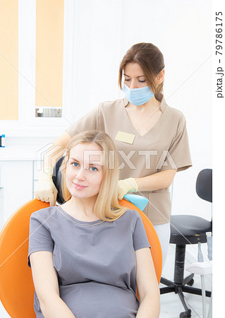 Young pregnant woman in a dental clinic, sitting in a treatment chair, a dentist's assistant puts on a protective napkin 79786175