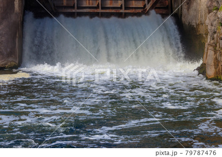 Flowing water with water spray from the open sluice gates of a small dam 79787476