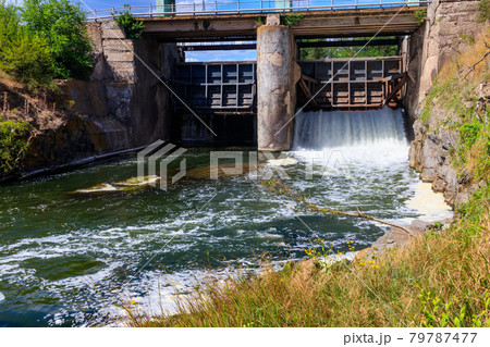 Flowing water with water spray from the open sluice gates of a small dam 79787477