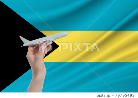 Airplane in hand with national flag of Bahamas. Travel to Bahamas 79795495