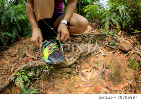 Woman trail runner tying shoelace on forest trail Woman trail runner tying shoelace on forest trail 79796897