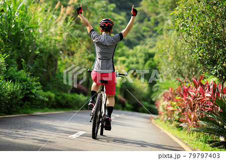 Woman no handed cycling on tropical park trail in summer Woman no handed cycling on tropical park trail in summer 79797403