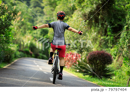 Woman no handed cycling on tropical park trail in summer 79797404
