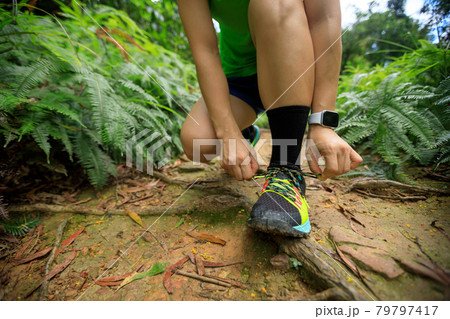 Woman trail runner tying shoelace on forest trail Woman trail runner tying shoelace on forest trail 79797417
