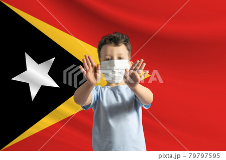 Little white boy in a protective mask on the background of the flag of East Timor. Makes a stop sign with his hands, stay at home East Timor Little white boy in a protective mask on the background of the flag of East Timor. Makes a stop sign with his hands, stay at home East Timor 79797595